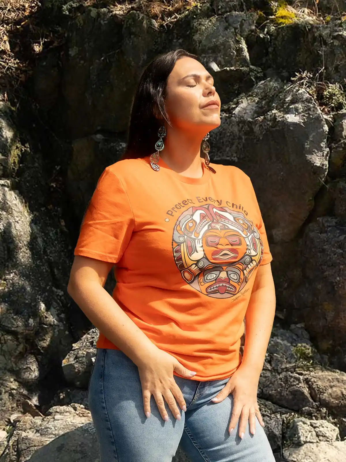 Woman wearing an orange t-shirt with a circular indigenous-style graphic and the words "Protect Every Child".